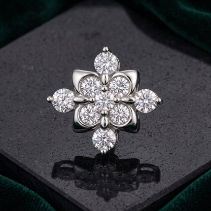 A silver-toned flower-shaped brooch with multiple clear round and marquise-cut stones, displayed on a dark reflective surface with a green velvet background.