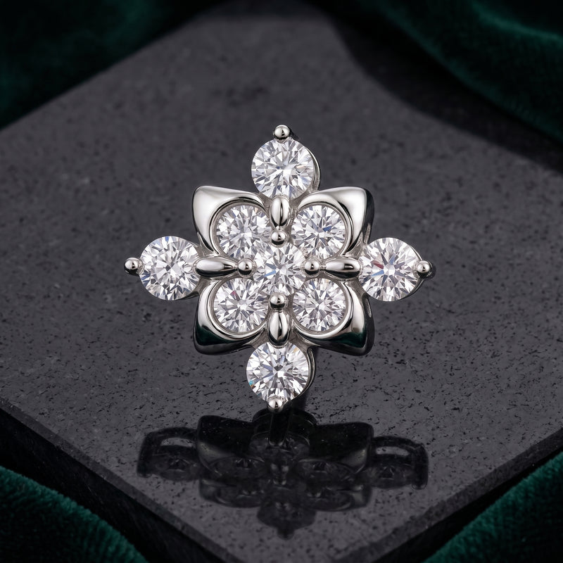 A silver-toned flower-shaped brooch with multiple clear round and marquise-cut stones, displayed on a dark reflective surface with a green velvet background.