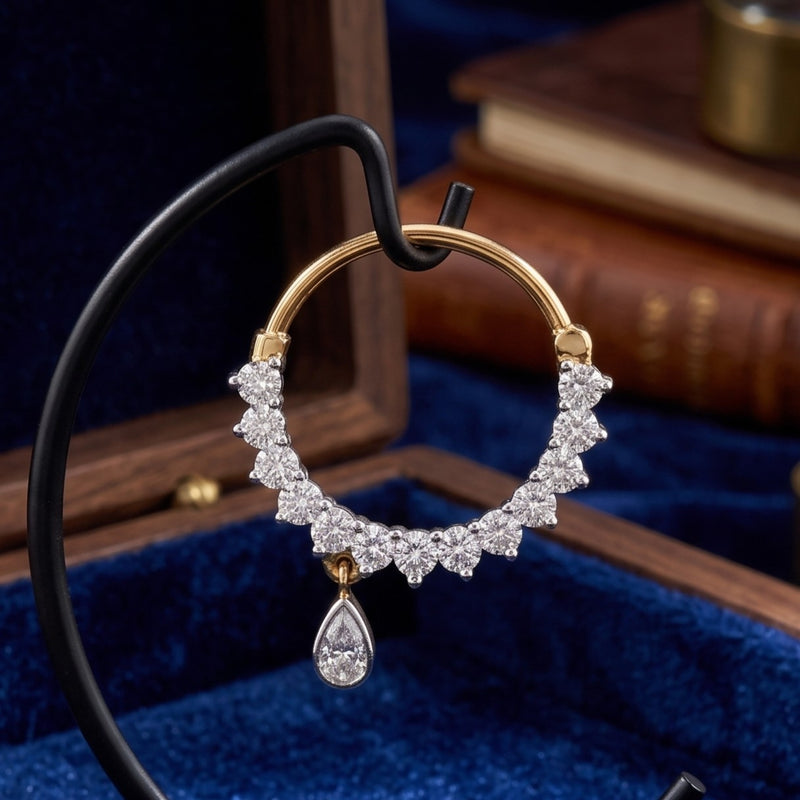 A gold and white diamond crescent hoop nosepin with a teardrop diamond pendant, displayed on a black jewelry stand inside a blue velvet box.