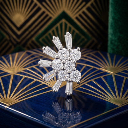 A sparkling Art Deco style nose pin featuring a cluster of round brilliant-cut diamonds surrounded by baguette-cut diamonds in a silver-toned setting, displayed on a blue and gold patterned box.