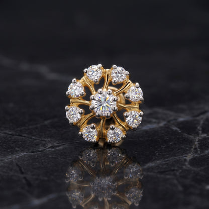 A gold flower-shaped ring with a central round diamond and surrounding smaller diamonds, displayed on a dark reflective surface.