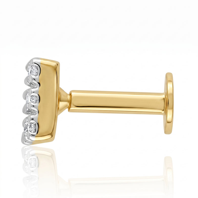 A close-up side view of a gold and white gold nosepin with a row of clear gemstones, set against a clean white background with a soft reflection below.