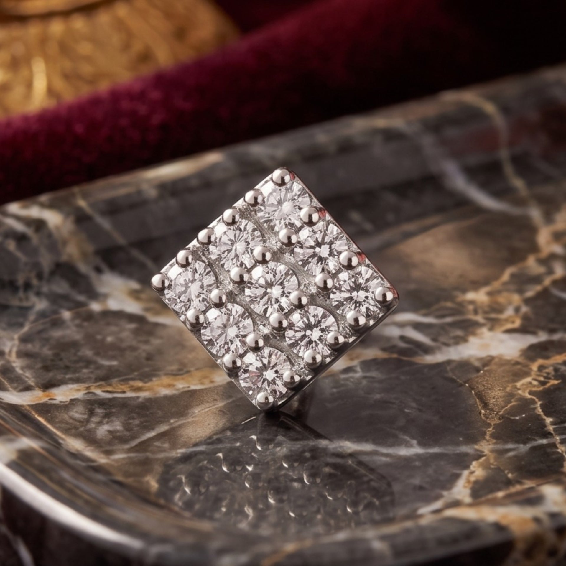 A square silver nosepin set with pavé diamonds, displayed on a polished black and gold marble slab with a dark red velvet background.