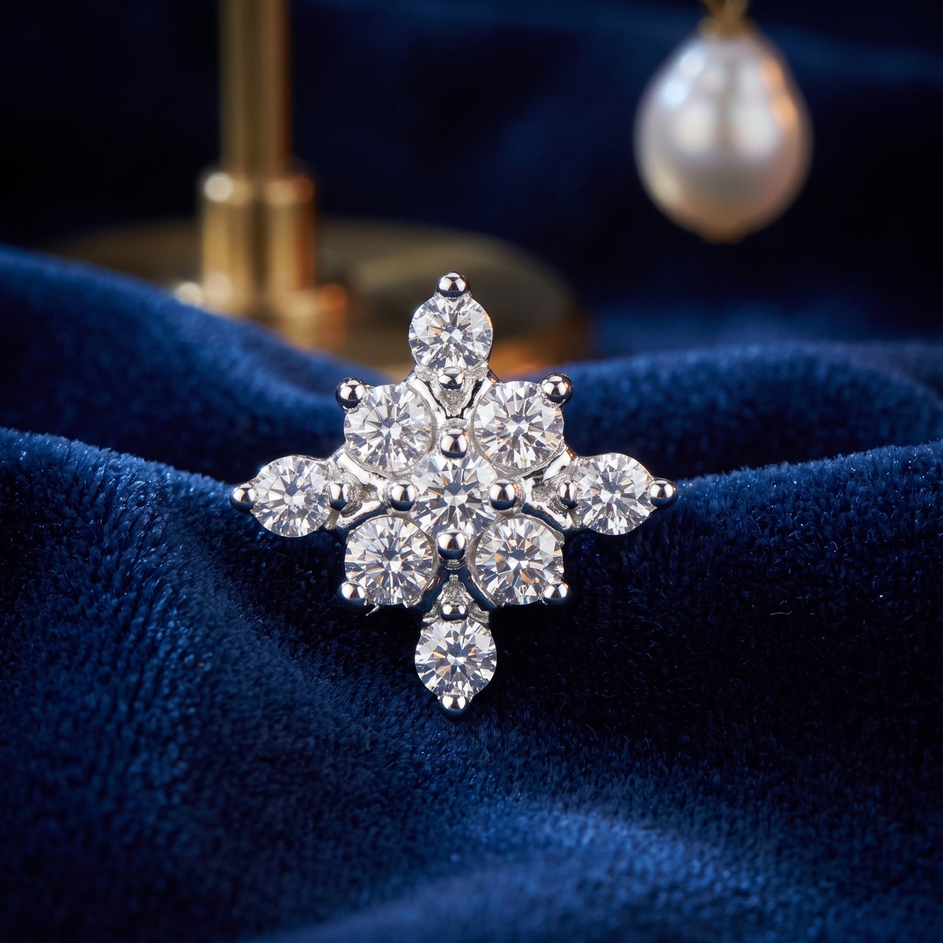 A snowflake-shaped silver ring set with clear round and marquise-cut gemstones, displayed on a textured dark blue velvet surface with a softly blurred pearl and gold stand in the background.