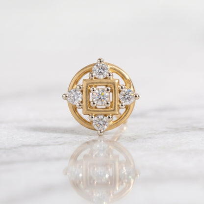 A yellow gold nose ring with a square and circular diamond setting, displayed on a light marble surface with a soft reflection.