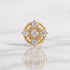 A yellow gold nose ring with a square and circular diamond setting, displayed on a light marble surface with a soft reflection.