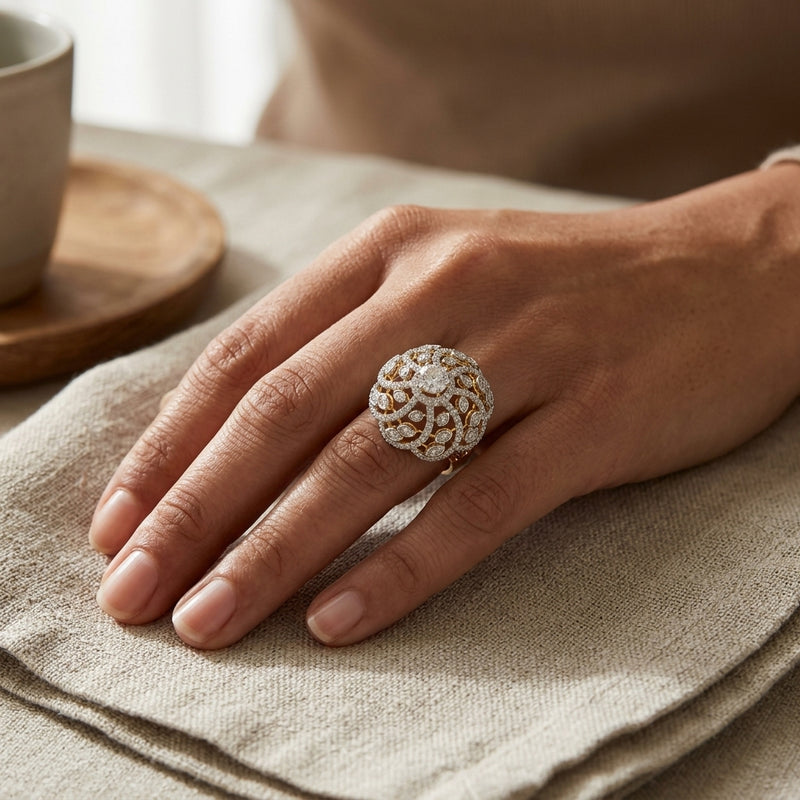 Hand wearing a decorative ring on a textured surface with a blurred cup in the background