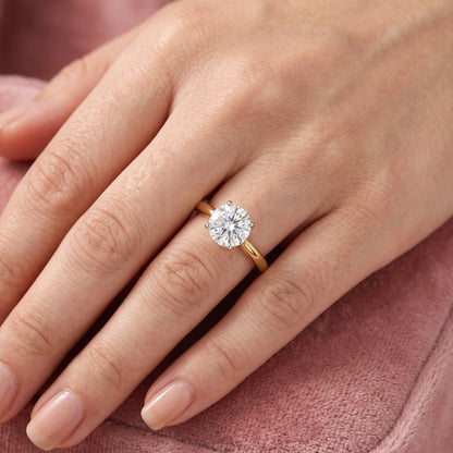 Gold ring with a diamond on a hand against a pink fabric background