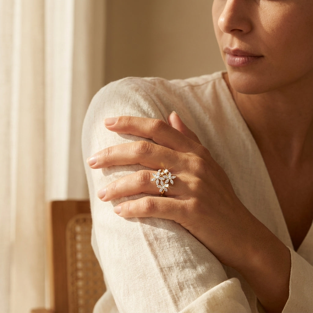 Woman wearing a delicate ring with floral design on her hand, sitting in a softly lit room.