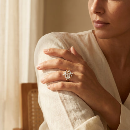 Woman wearing a delicate ring with floral design on her hand, sitting in a softly lit room.