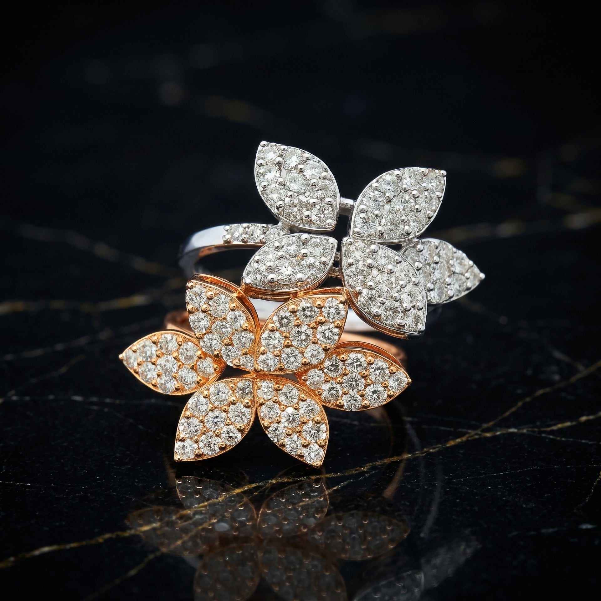 Two diamond-encrusted flower-shaped rings on a dark surface