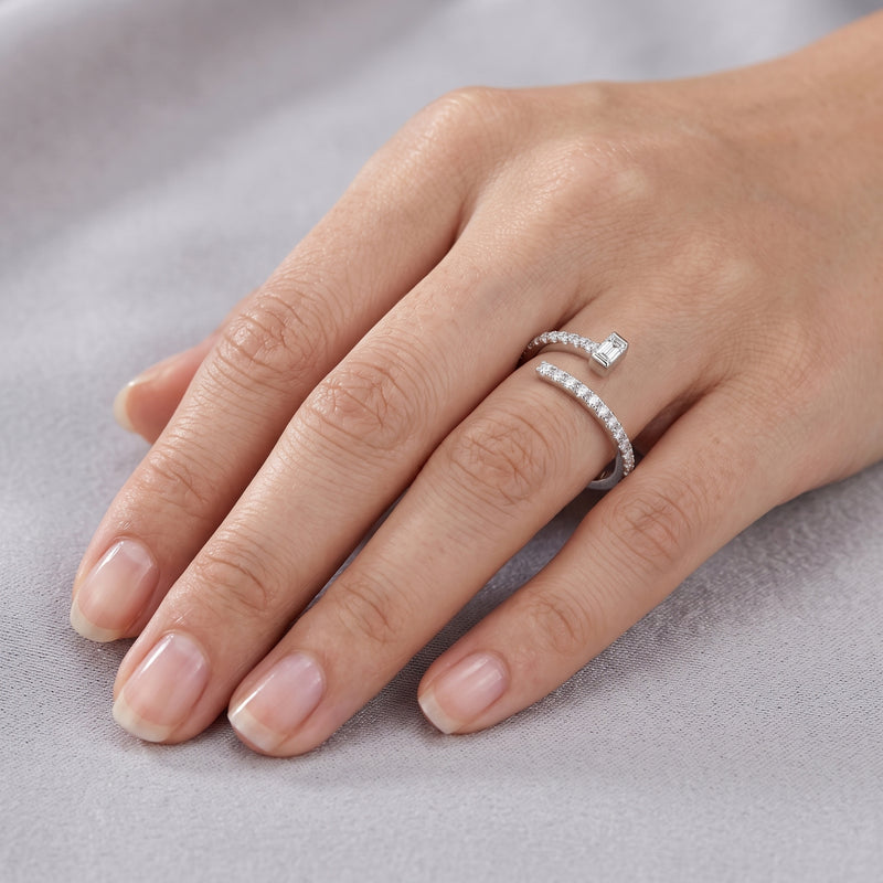 Hand wearing a silver ring with a diamond on a light gray background