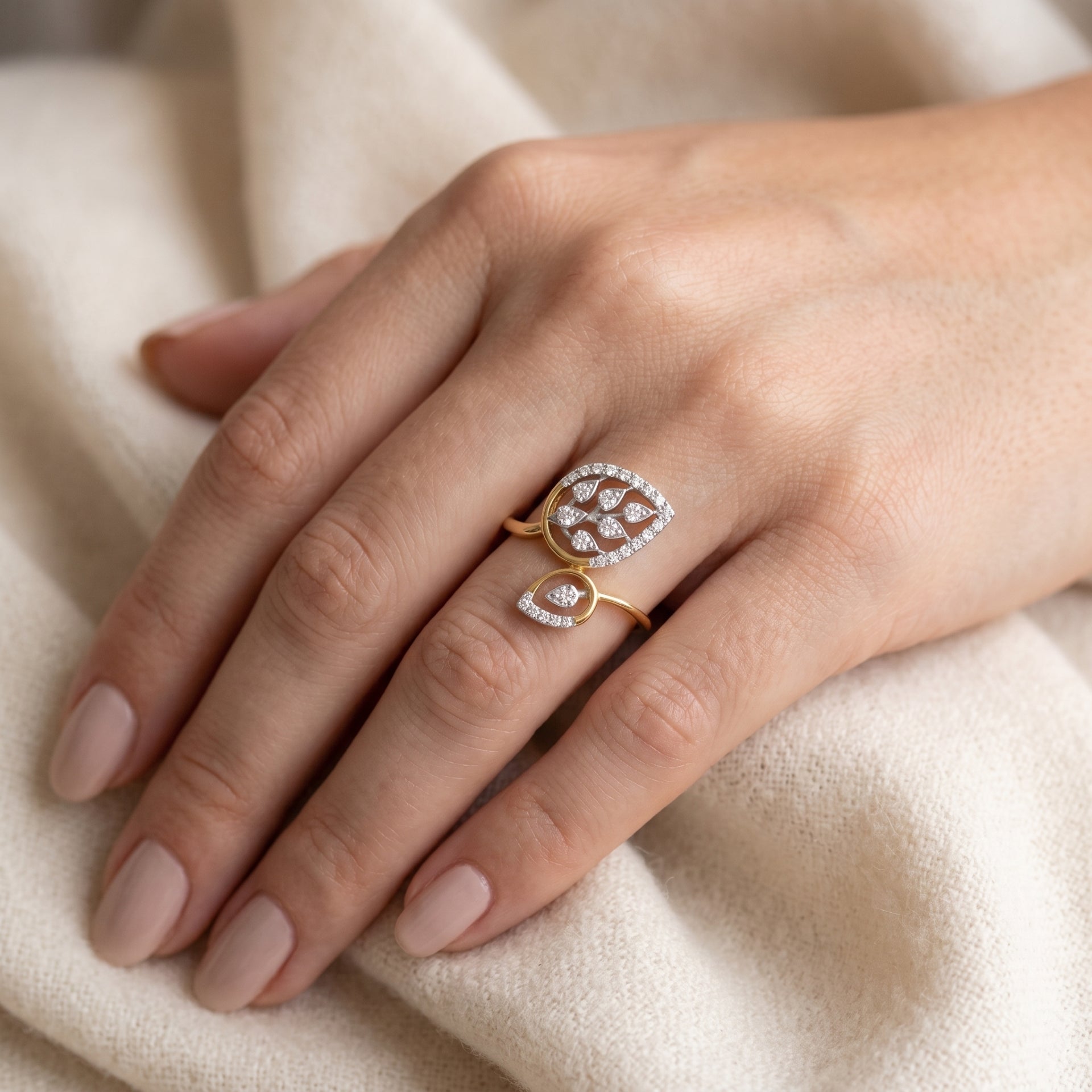Close-up of a hand wearing a gold ring with a diamond design on a beige fabric background