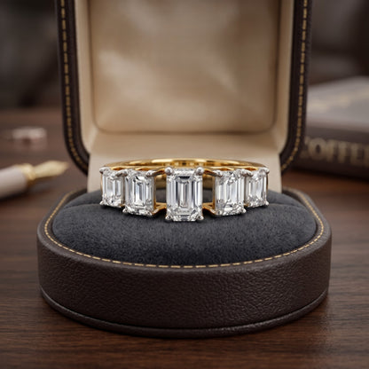 Gold ring with emerald-cut diamonds on a dark cushion in a jewelry box.