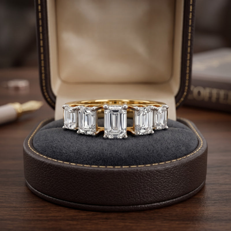 Gold ring with emerald-cut diamonds on a dark cushion in a jewelry box.
