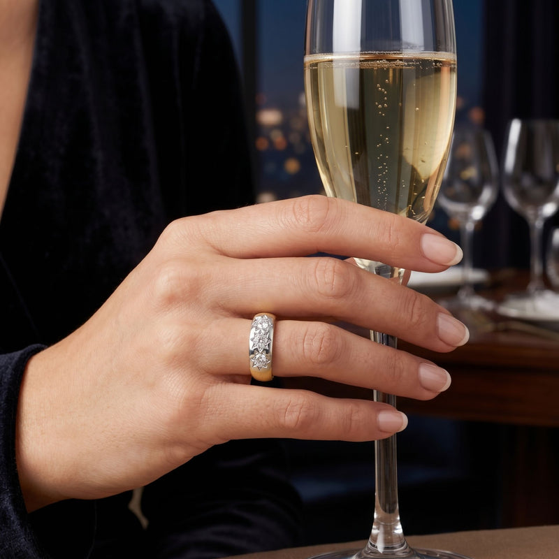 Hand wearing a gold ring featuring a sparkling lab-grown diamond while holding a champagne glass.