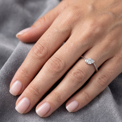 Hand wearing a diamond ring on a gray fabric background