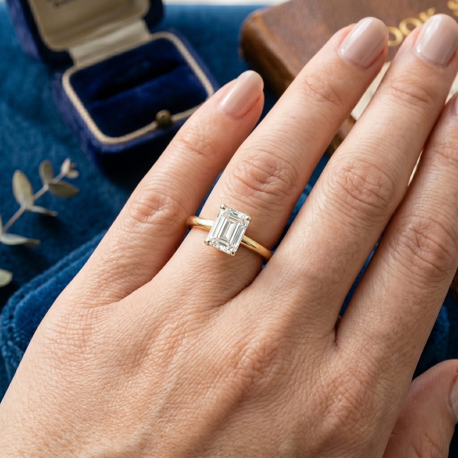 Hand wearing a gold ring with a diamond on a blue fabric background