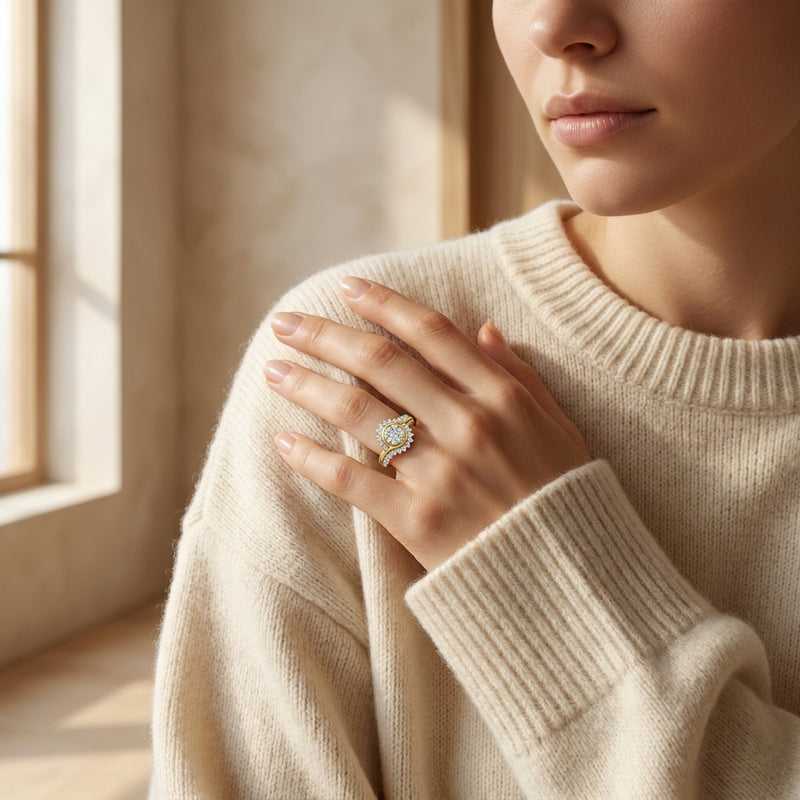 Woman wearing a beige sweater with a diamond ring on her finger, sitting by a window.