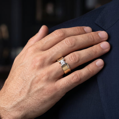 Hand wearing a gold ring with a diamond on a dark background