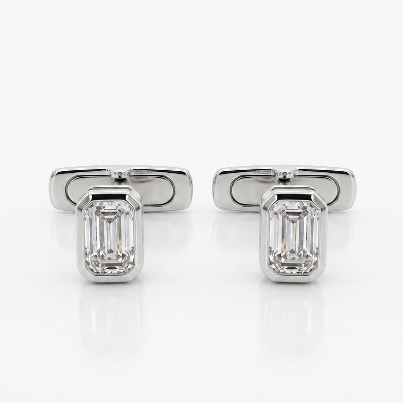 A pair of silver-toned cufflinks, each featuring an emerald-cut clear gemstone in a polished rectangular setting, displayed on a clean white reflective surface.