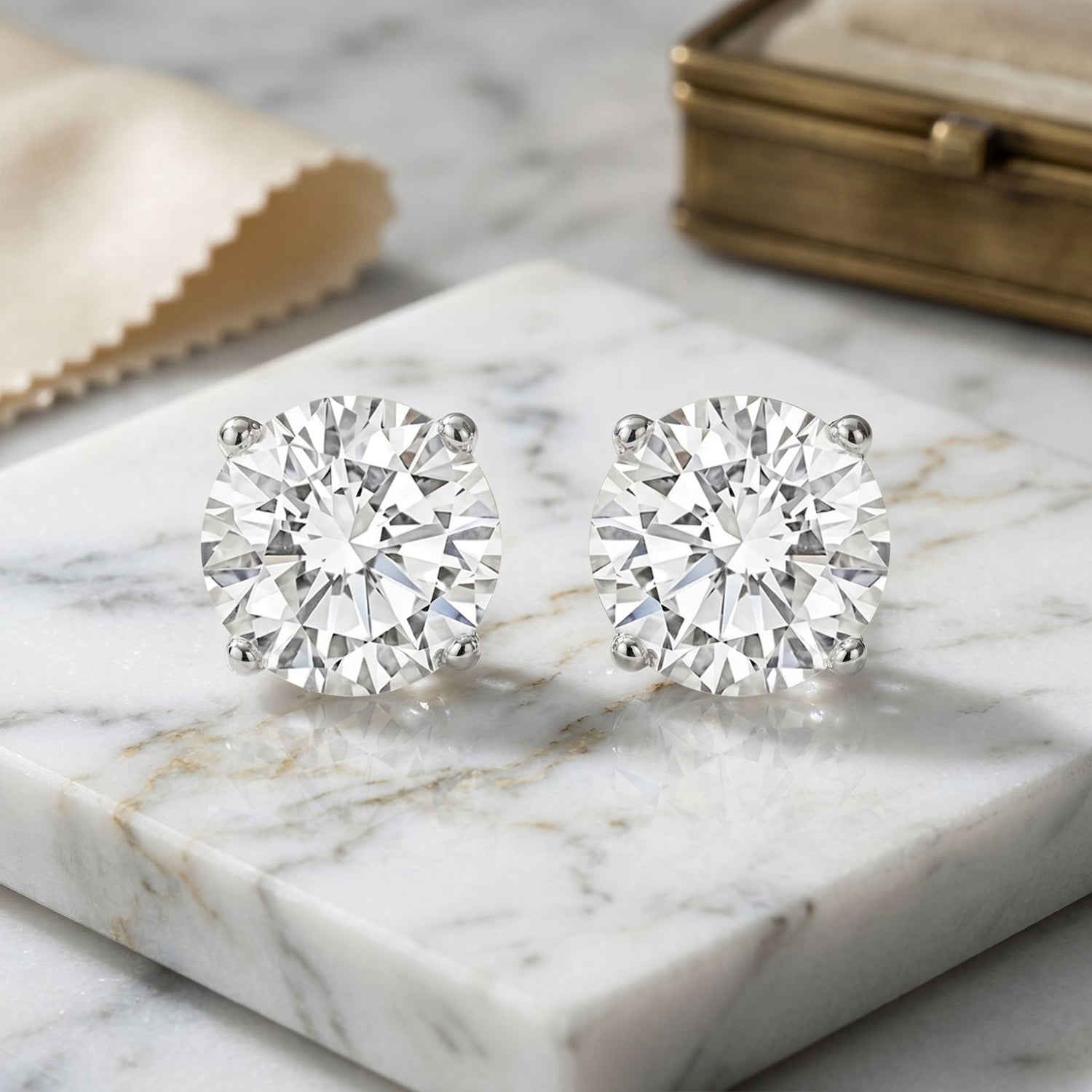 Pair of diamond stud earrings on a marble surface with a gold box in the background.