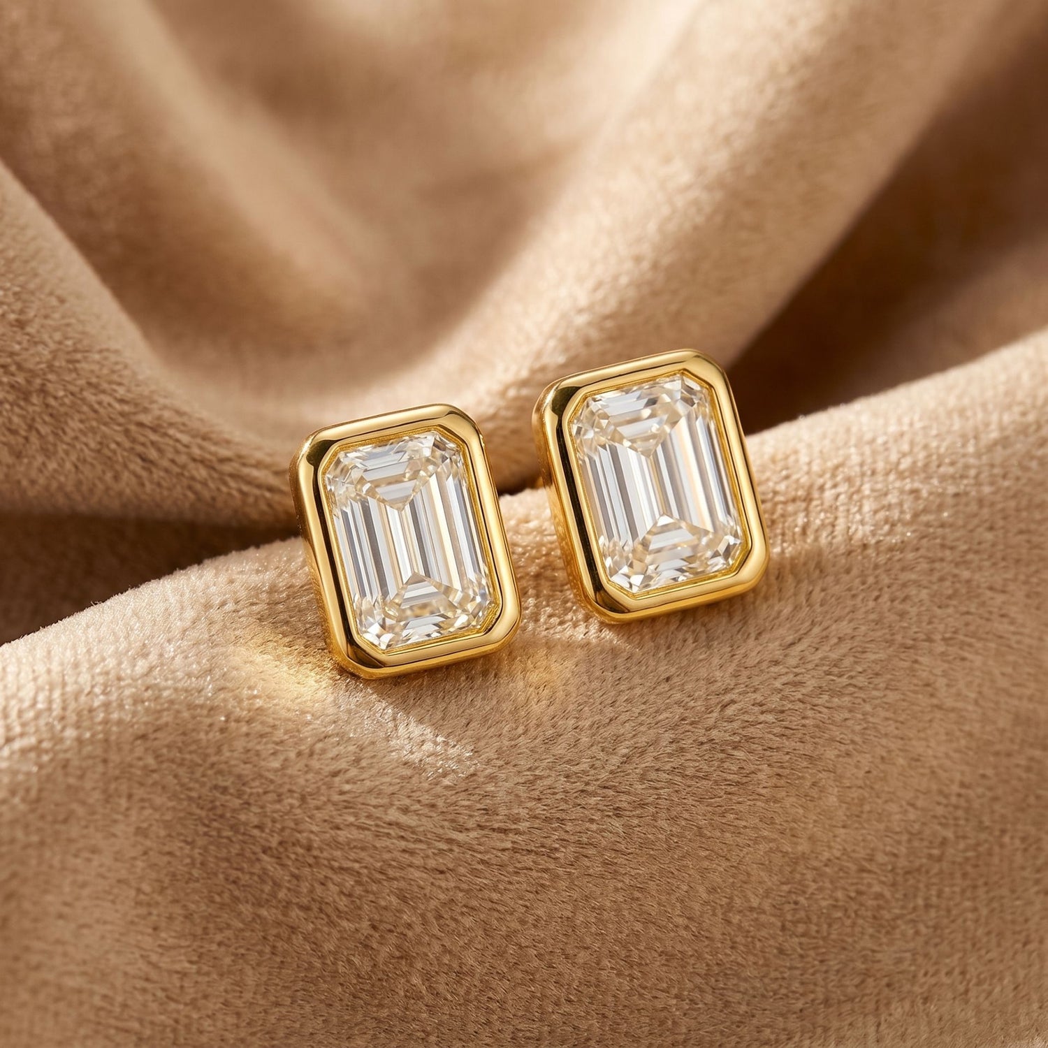 Emerald cut lab grown diamond stud earrings on a beige satin background
