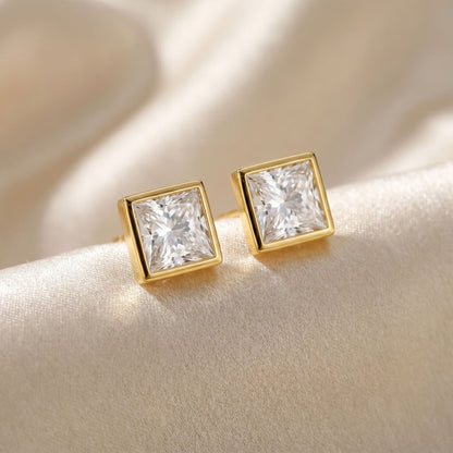 Gold square-cut stud earrings with square shaped diamond in the centre on a soft beige background