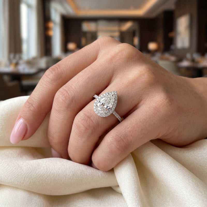 Close-up of a hand wearing a diamond ring with a blurred indoor background