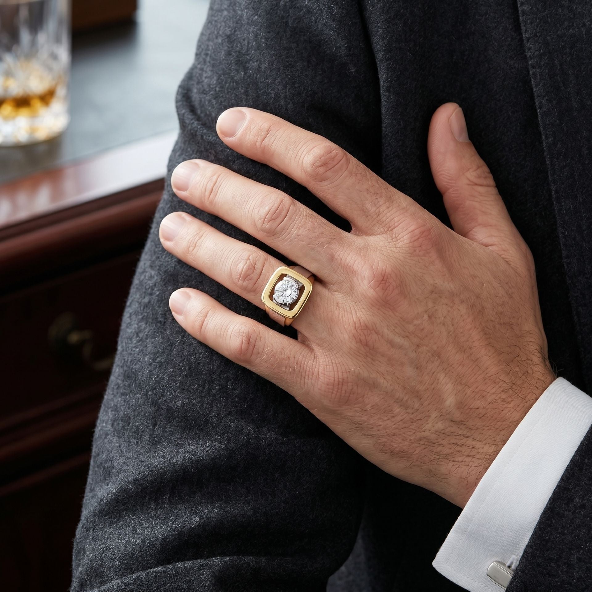 Hand wearing a gold ring with a diamond, resting on a gray suit jacket.