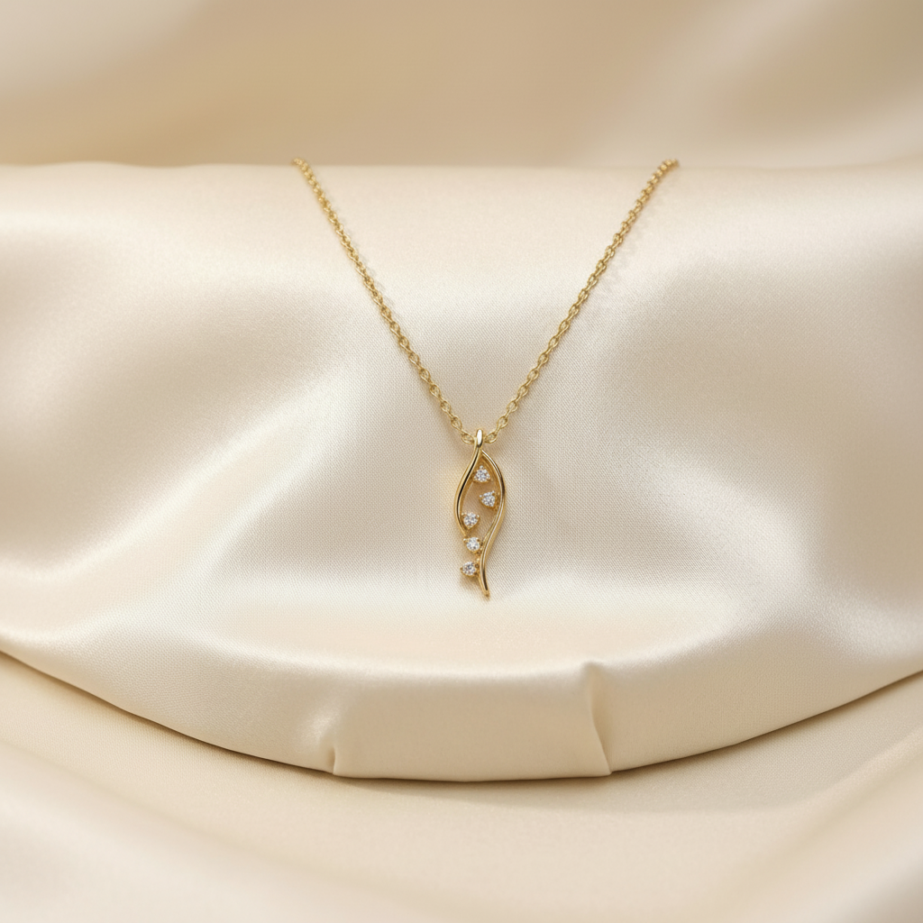 Gold necklace with a leaf-shaped pendant on a beige satin background