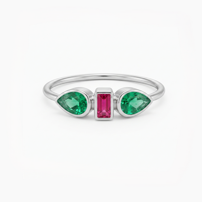 A silver ring featuring two green marquise-cut gemstones on either side of a central rectangular pink gemstone, set against a plain white background.