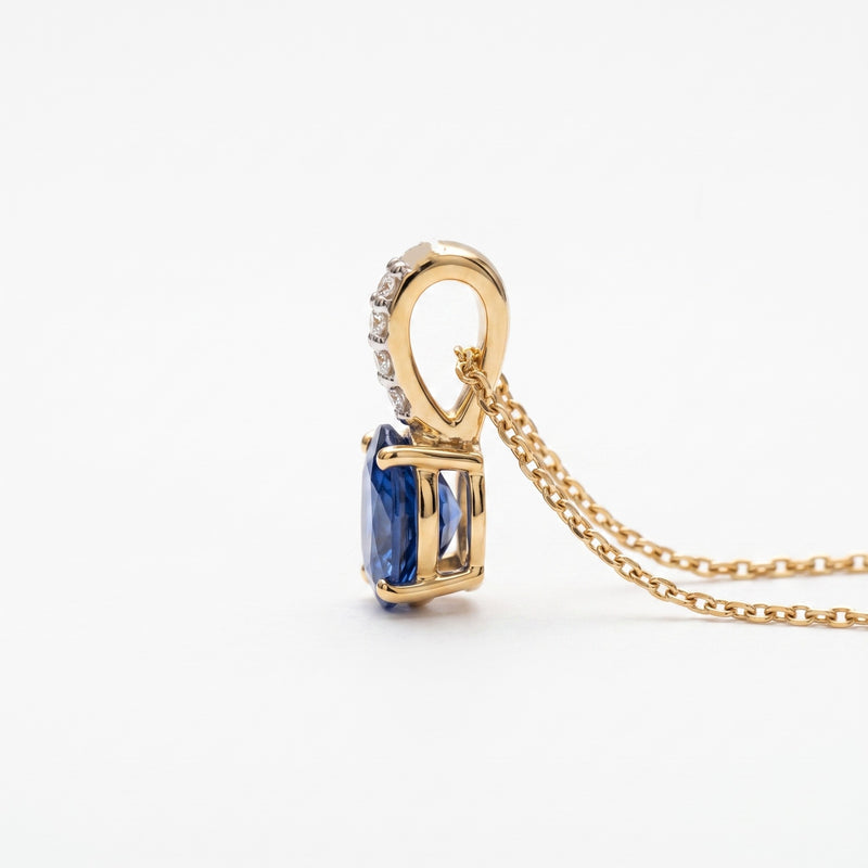 Side view of a gold necklace with an oval blue sapphire pendant and a pavé-set diamond accent bar, on a wite background
