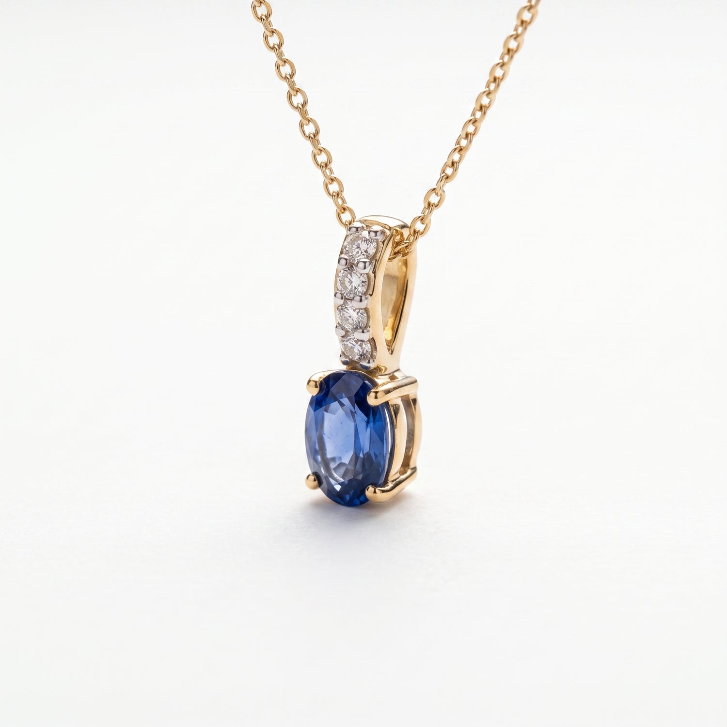 A gold necklace with an oval blue sapphire pendant and a pavé-set diamond accent bar, on a wite background