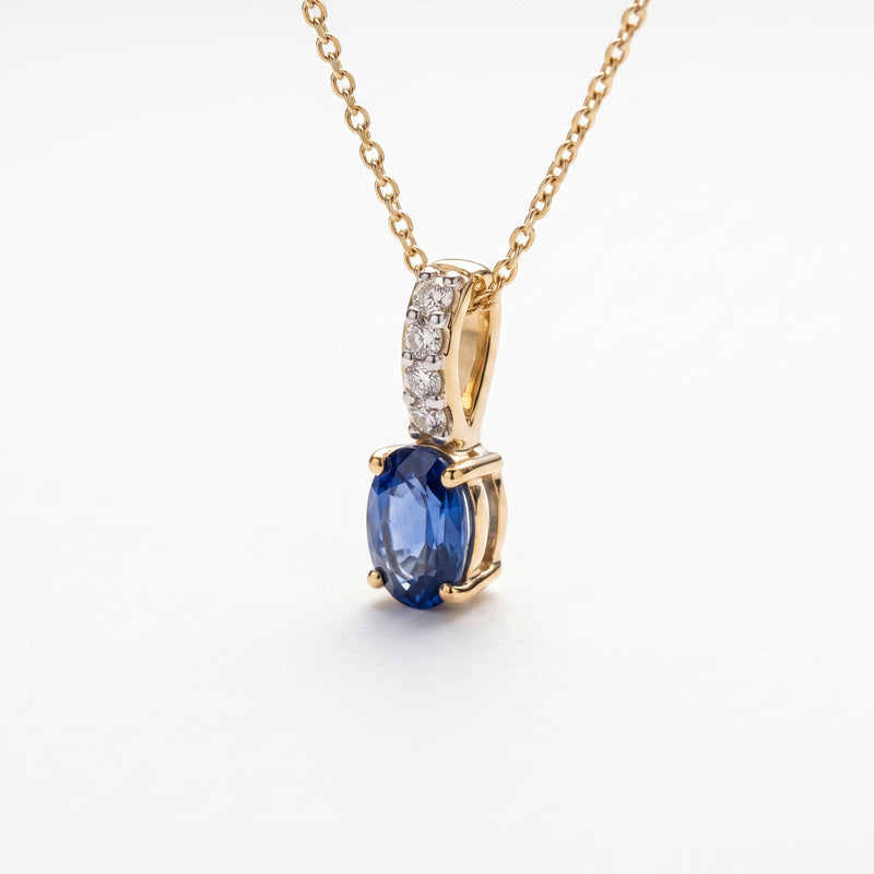A gold necklace with an oval blue sapphire pendant and a pavé-set diamond accent bar, on a wite background