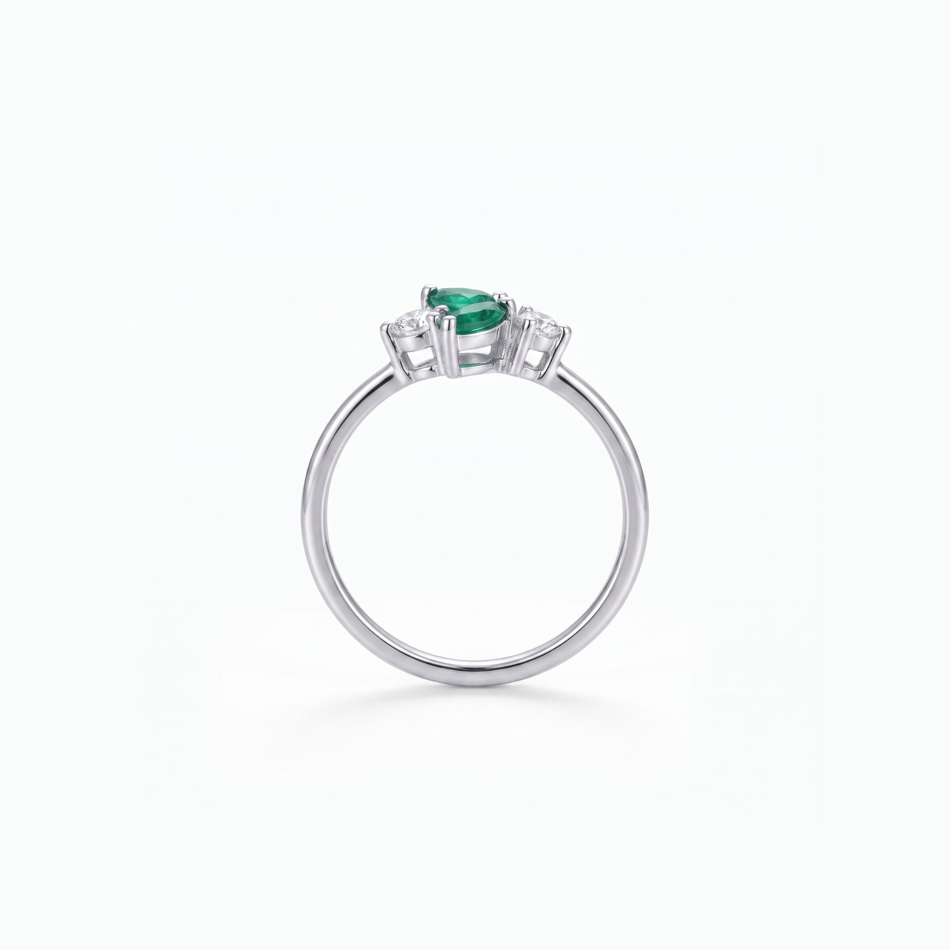 A silver ring featuring a pear-cut green emerald center stone and small clear accent stones on either side, shown on a clean white background.