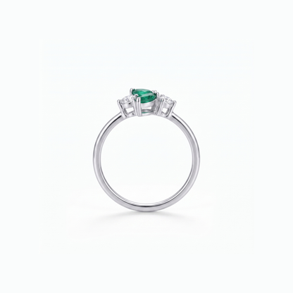 A silver ring featuring a pear-cut green emerald center stone and small clear accent stones on either side, shown on a clean white background.