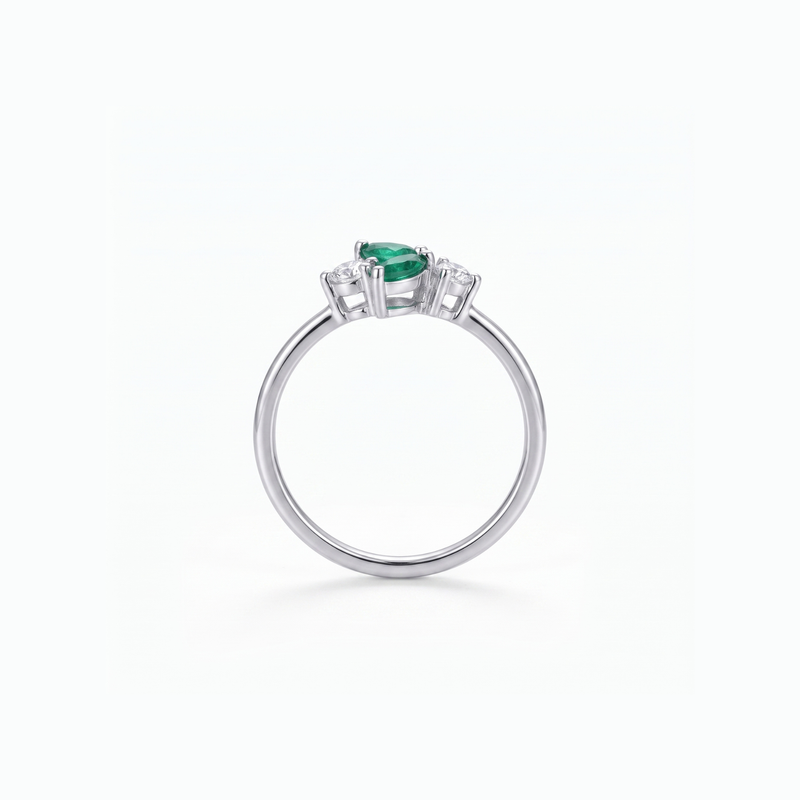 A silver ring featuring a pear-cut green emerald center stone and small clear accent stones on either side, shown on a clean white background.
