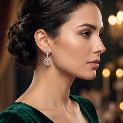 A close-up side profile of a woman wearing a teardrop-shaped silver dangle earring adorned with sparkling clear stones, set against a softly blurred dark background with warm bokeh lights.