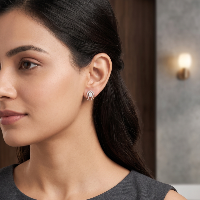 A close-up of a woman wearing a small teardrop-shaped stud earring with a silver-toned setting and clear stones, shown in profile against an indoor background.