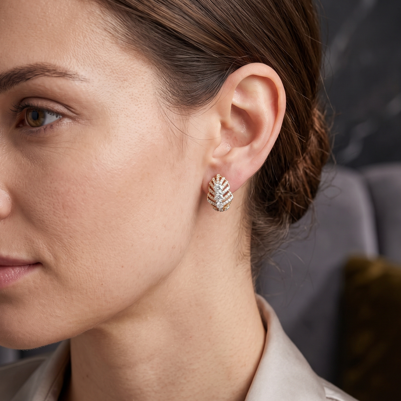 A close-up side profile of a woman wearing a small gold leaf-shaped stud earring adorned with clear crystals.