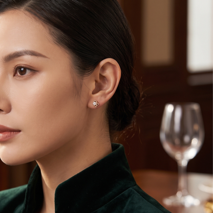 A close-up of a woman wearing a small round diamond stud earring, shown in profile against a warm, dark background with a blurred wine glass.