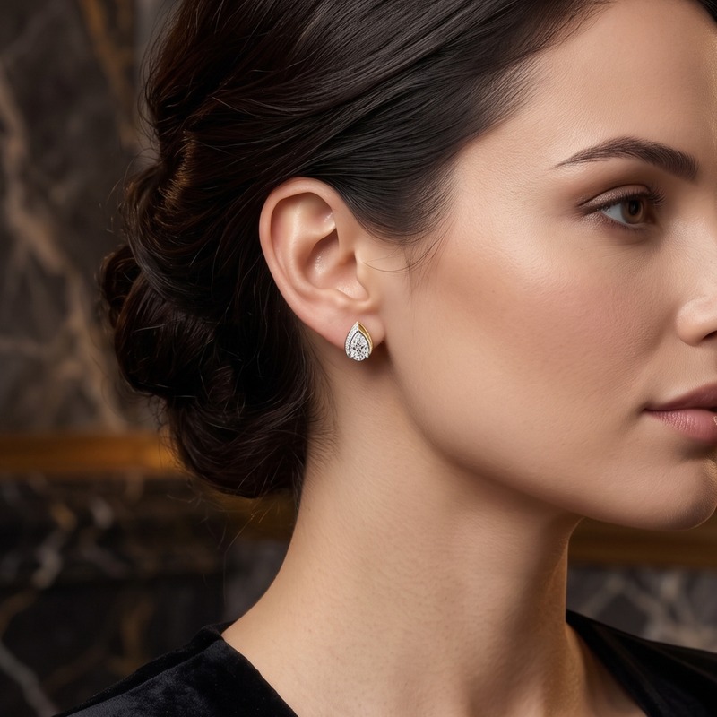 A close-up side profile of a woman wearing a small teardrop-shaped diamond stud earring in a silver setting, with a dark hair bun and a blurred dark marble background.