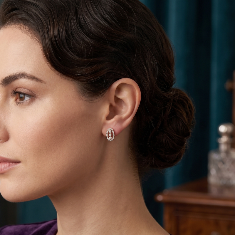 A close-up side profile of a woman with dark hair in an updo, wearing a small oval stud earring with a halo of clear stones and a central pink gemstone, set against a dark teal background.