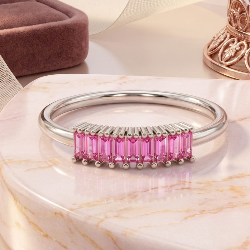 A polished silver-toned bangle bracelet featuring a curved row of bright pink rectangular baguette gemstones, displayed on a white marble surface.