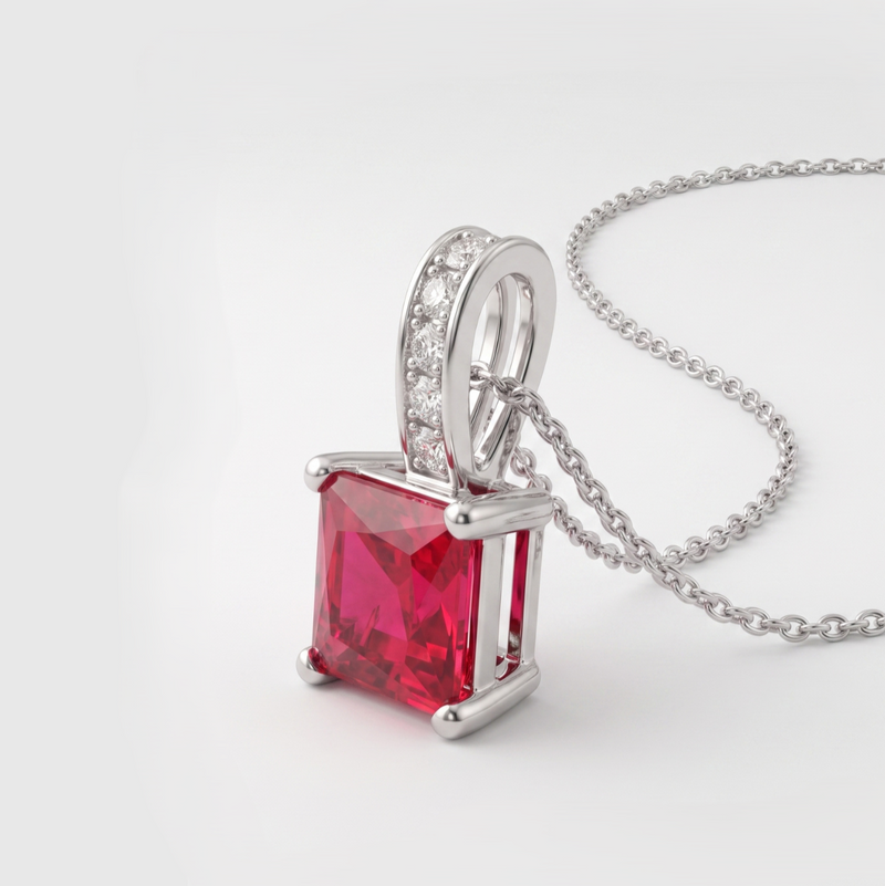 A silver pendant necklace featuring a square-cut red gemstone and a silver bail adorned with small clear stones, shown on a clean white background.