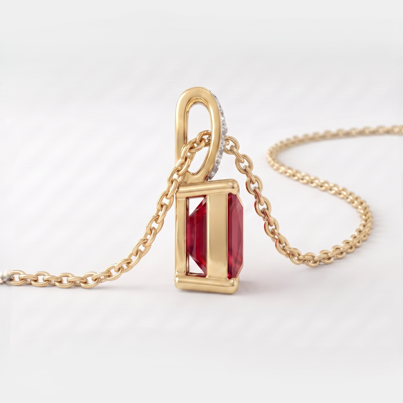 A gold pendant necklace featuring a rectangular red gemstone in a gold frame, suspended from a gold chain on a light gray background.