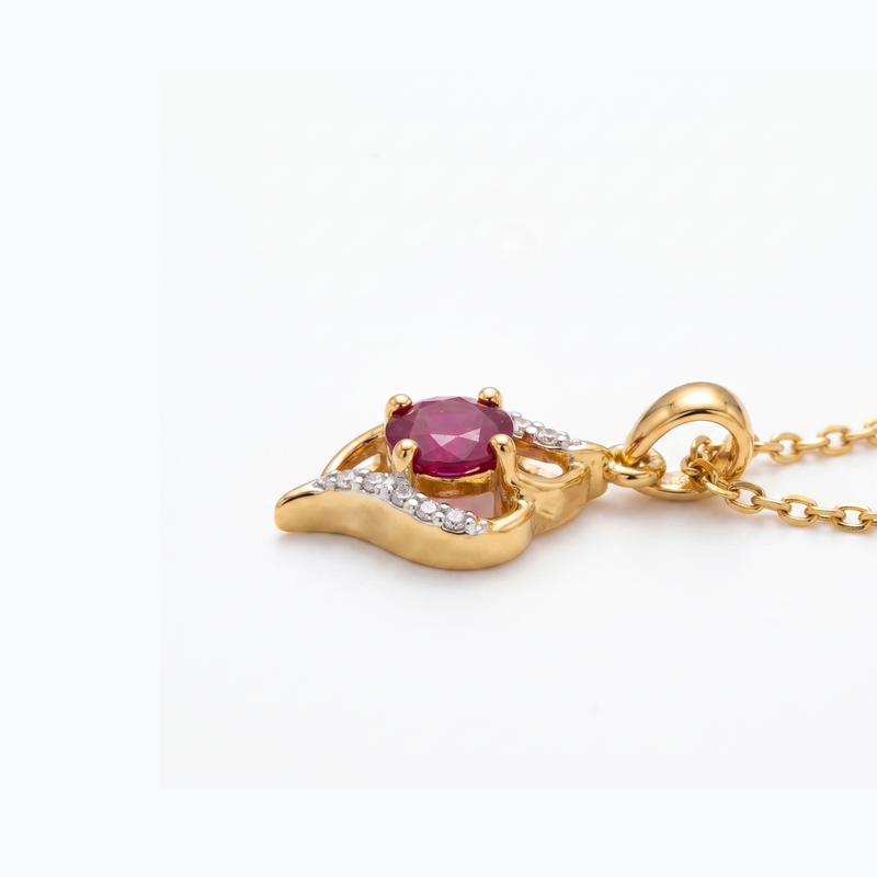 A gold pendant necklace featuring a central round-cut pinkish-red gemstone, accented by small clear stones along a curved setting, suspended from a gold chain against a plain white background.