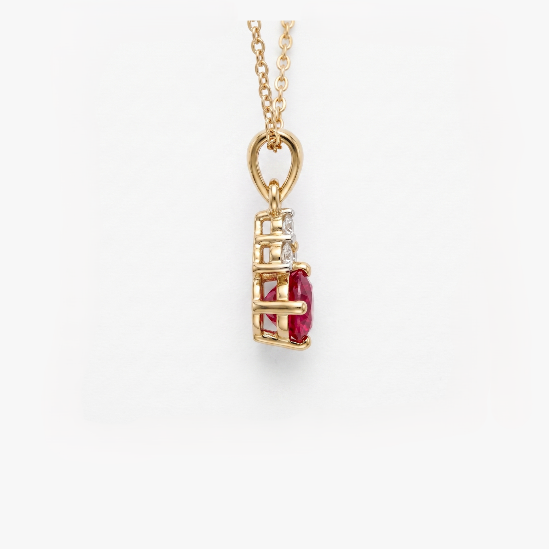 A gold pendant necklace featuring a vertical setting with a prominent oval-cut red ruby center stone and a small clear diamond beside it, suspended from a delicate gold chain against a clean white background.