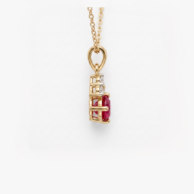 A gold pendant necklace featuring a vertical setting with a prominent oval-cut red ruby center stone and a small clear diamond beside it, suspended from a delicate gold chain against a clean white background.
